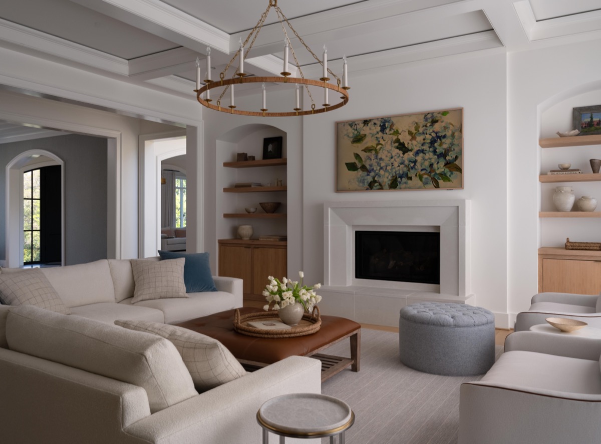Bright contemporary living room with a white sectional sofa, circular bronze chandelier, and a fireplace framed by built-in shelves.