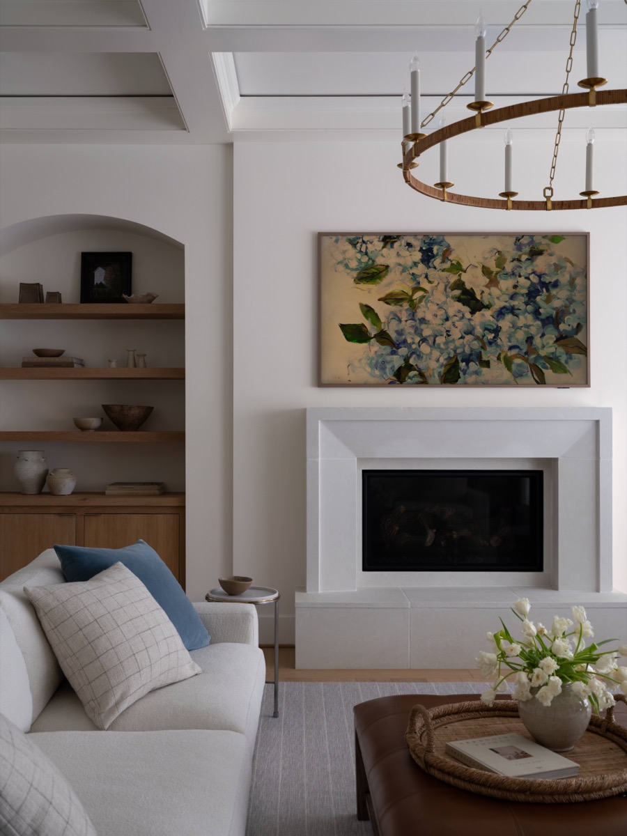 Living room with a white fireplace, a large abstract floral painting above, and a brass circular chandelier overhead.